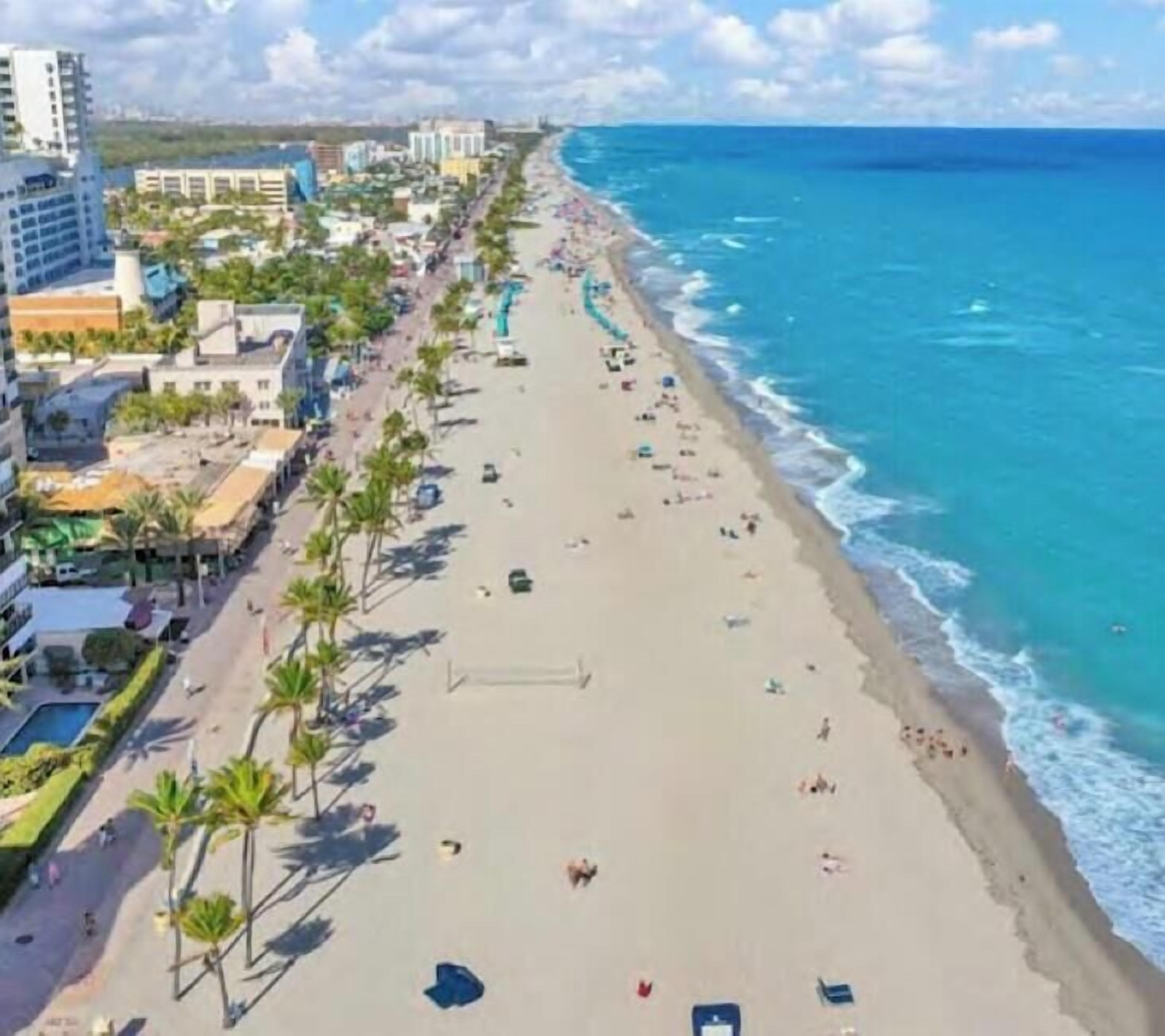 Un paysage urbain côtier avec une vaste plage, une promenade bordée de palmiers et des bâtiments situés à proximité du rivage.