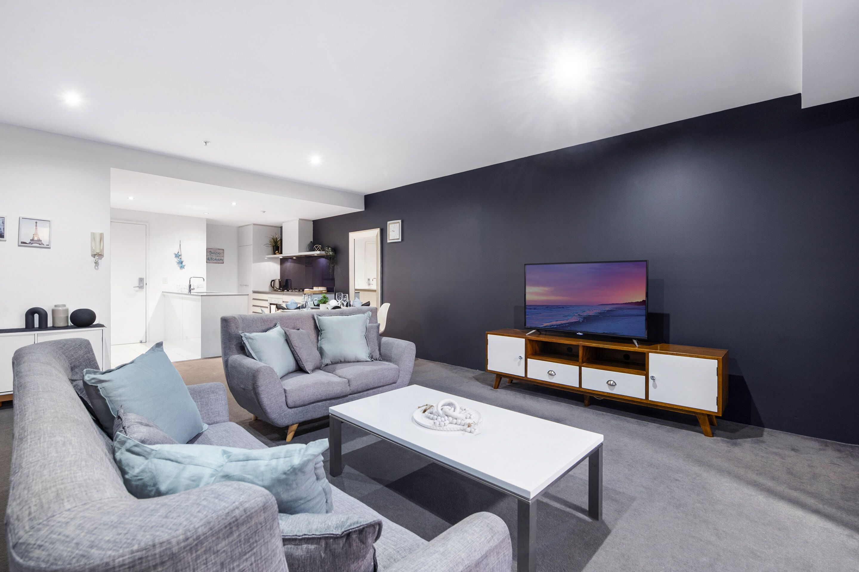 A modern living room with a grey sofa, a white coffee table, and a TV on a wooden cabinet.
