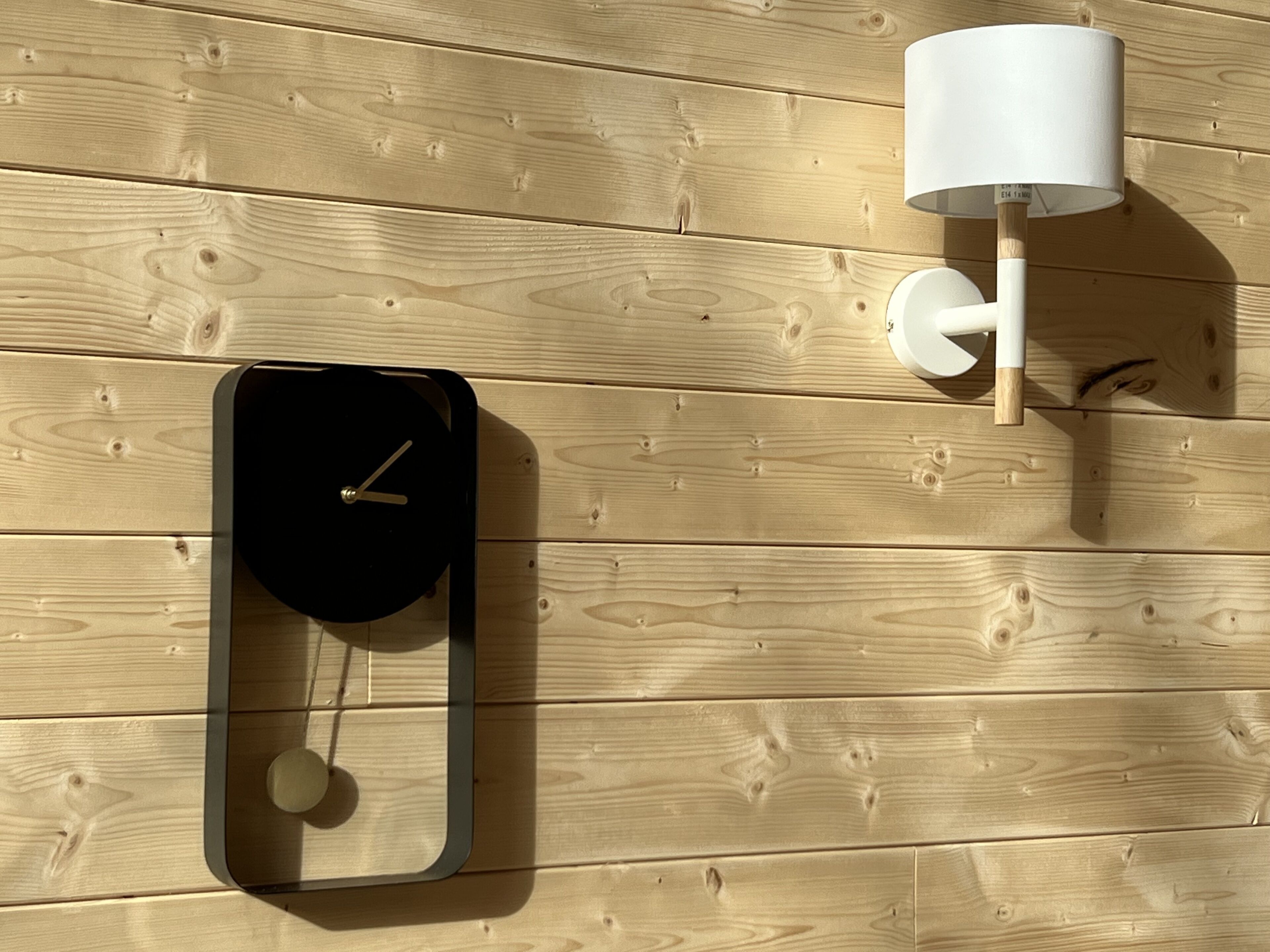 Un orologio a parete dal design minimalista, una lampada da parete e un pannello di legno a mo' di sfondo.