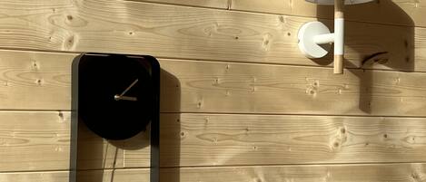 Un orologio a parete dal design minimalista, una lampada da parete e un pannello di legno a mo' di sfondo.