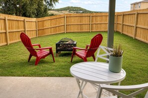 A backyard with a wooden fence, two red chairs, a small table, and a potted plant.