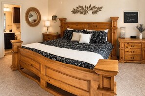 A bedroom with a wooden bed, a nightstand, a dresser, a mirror, and a wall with decorative items.
