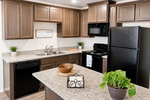 Une cuisine avec des meubles de rangement en bois, un réfrigérateur noir, un four à micro-ondes, une cuisinière et un évier.