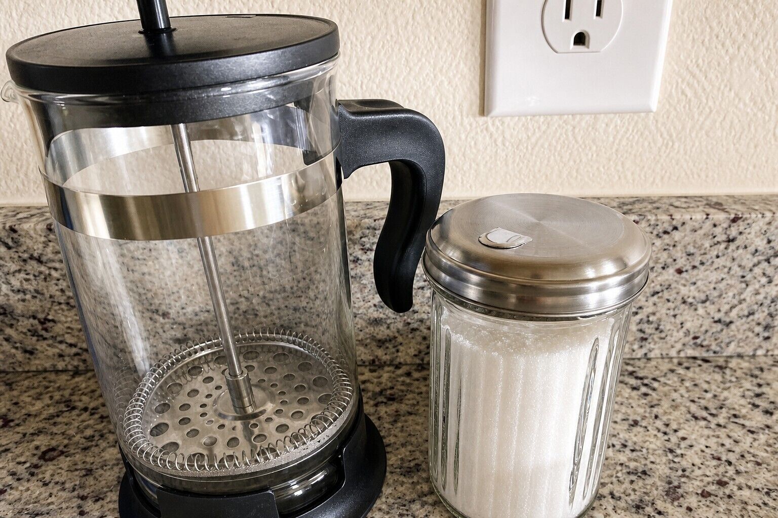 Een cafetière en een zoutstrooier op een granieten aanrecht.