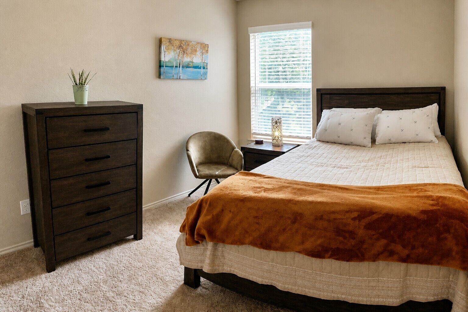 Un dormitorio con cama, cómoda, silla, ventana con persianas y un cuadro en la pared.
