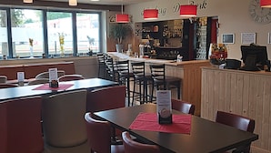 A restaurant interior with booths and tables, a bar area, and a view of the outside. - De Berk Hotel (Essen)