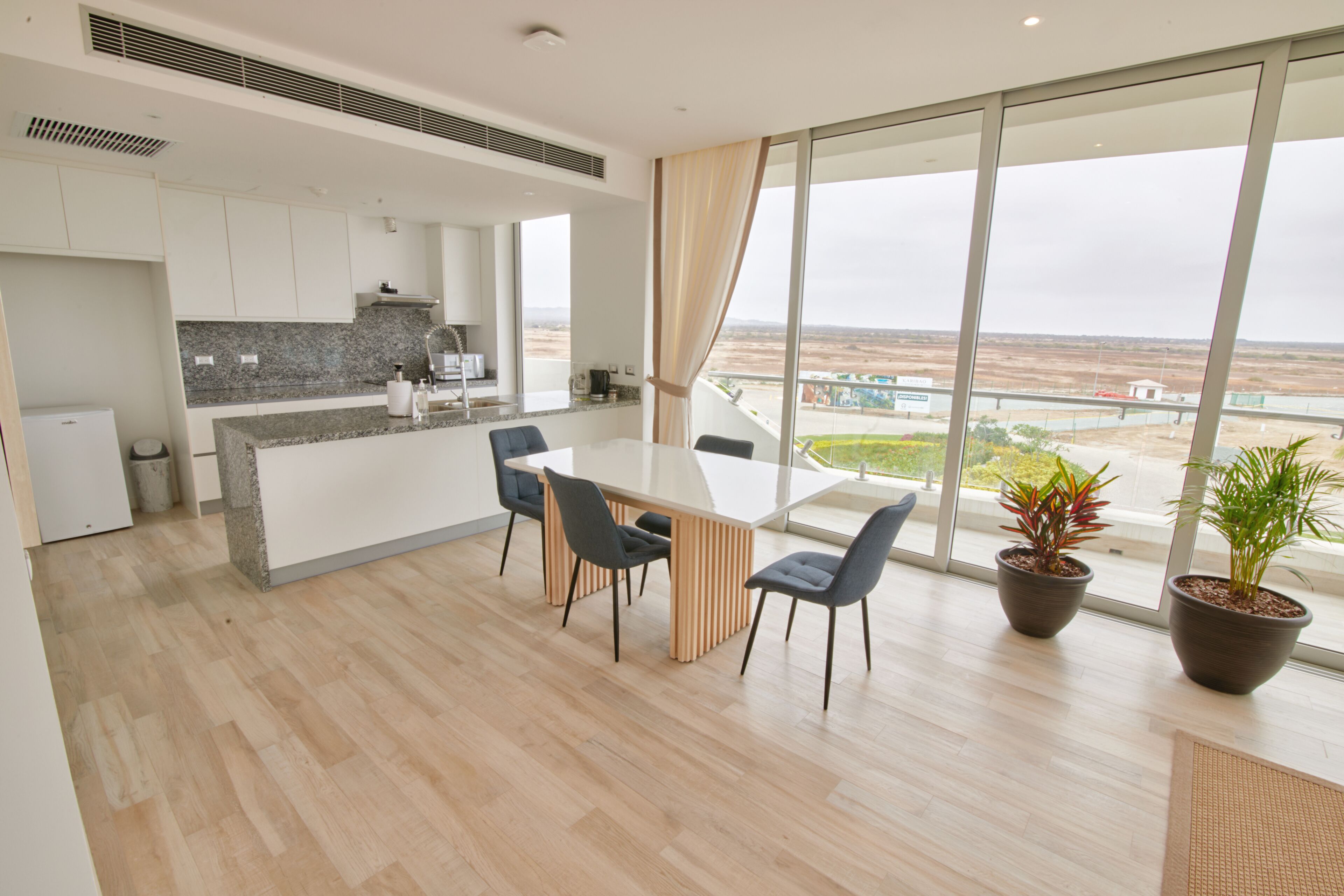 A modern kitchen with granite countertops, a dining area with a glass table and chairs, and large windows offering a view of the landscape.