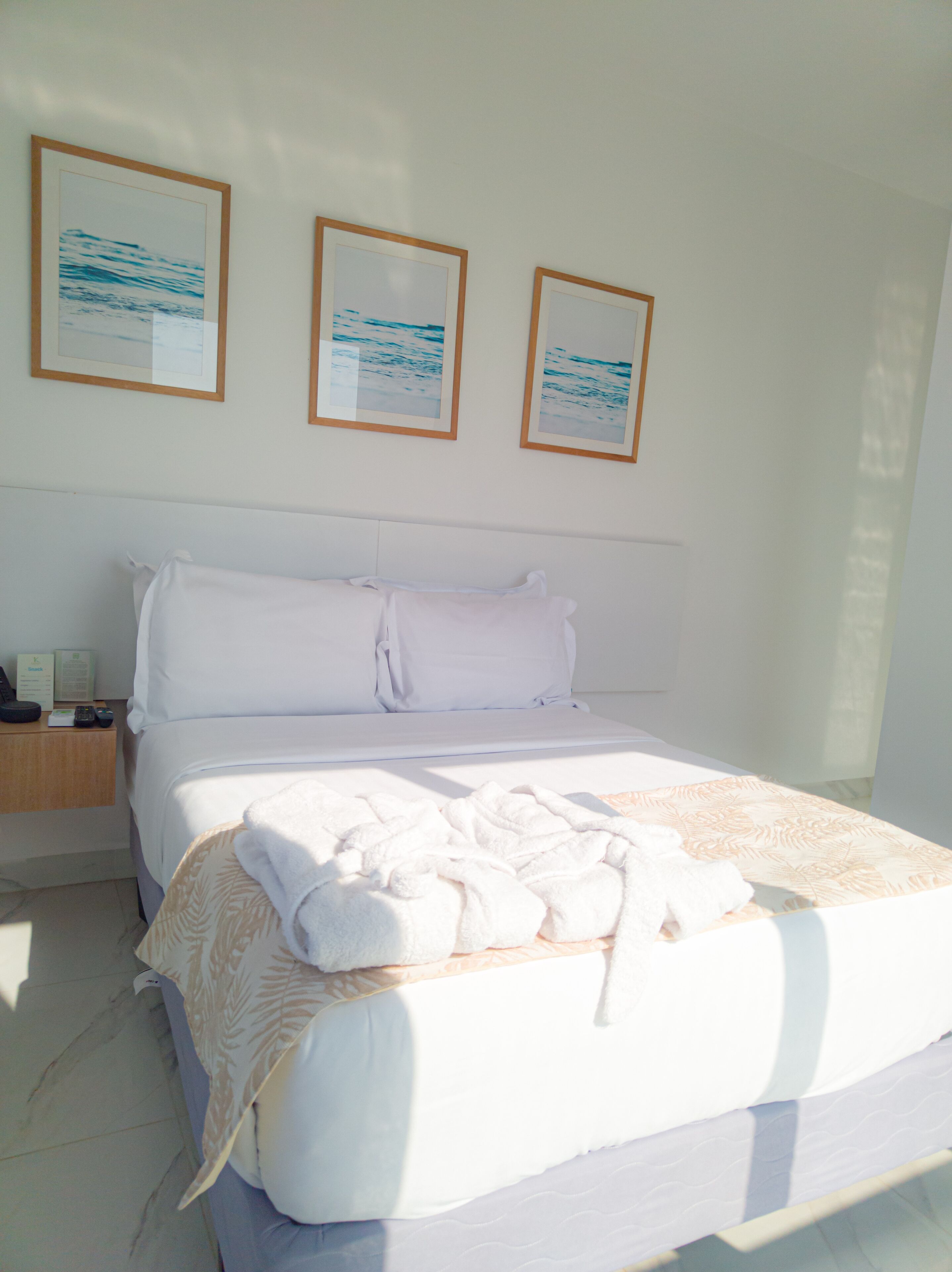 A hotel room with a large bed, white bedding, a wooden nightstand with a lamp, and three framed pictures on the wall.