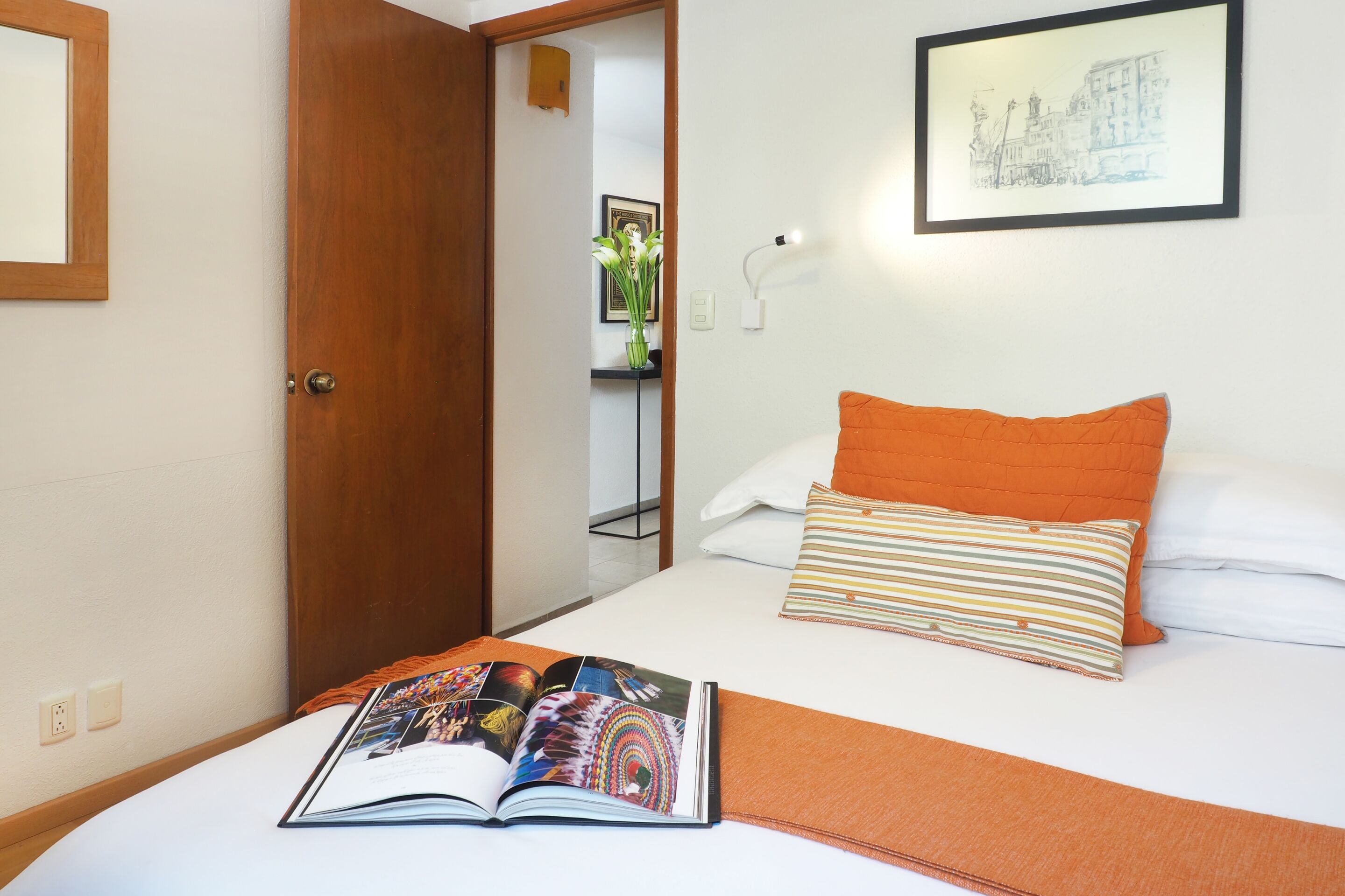 Una camera d'albergo con un letto, un libro, un quadro appeso alla parete e una porta che dà su un'altra stanza.