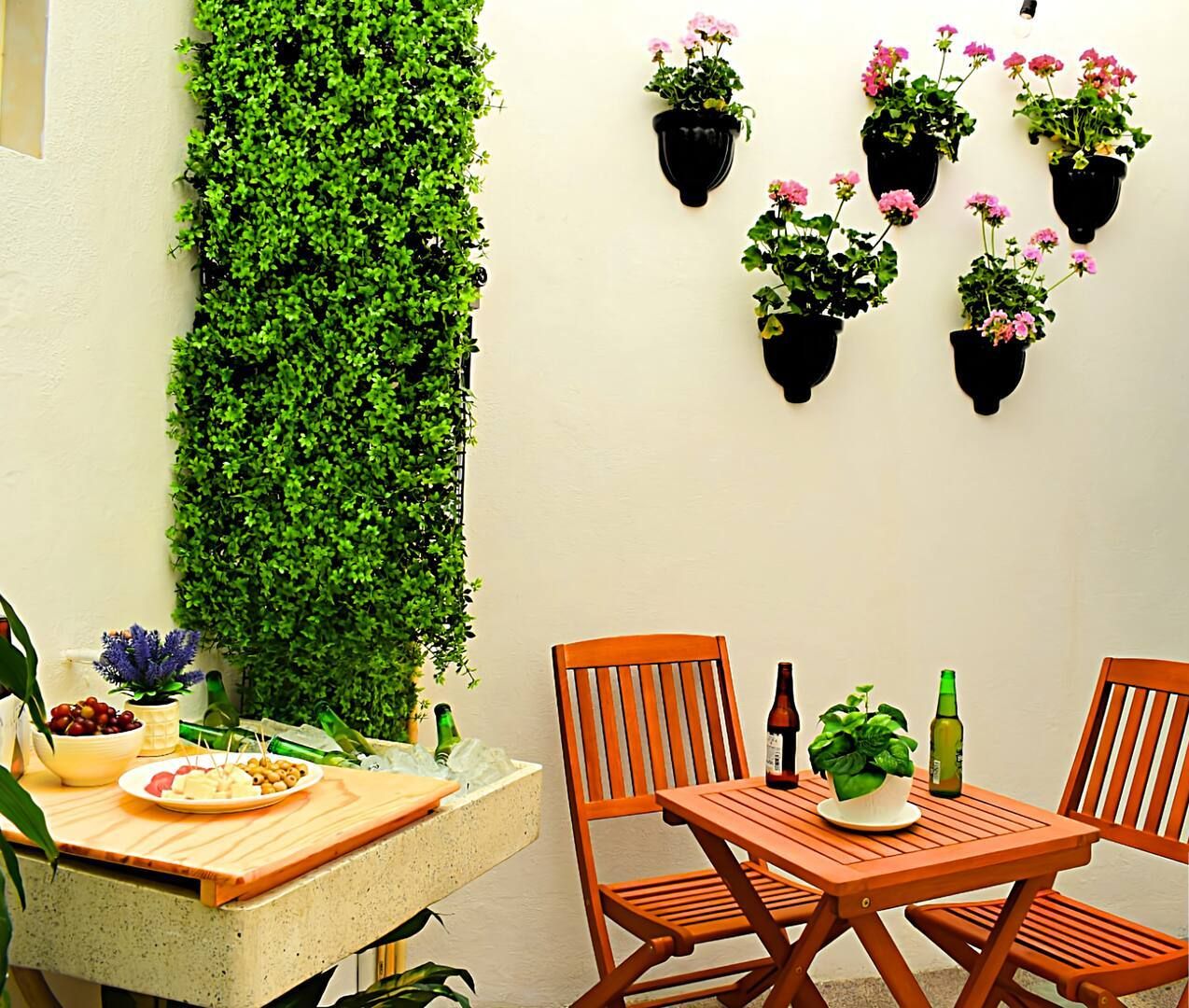 A small outdoor dining area with a wooden table and two chairs, surrounded by potted plants and a vertical garden.