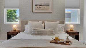 Un dormitorio ordenado con una cama grande, dos mesitas de noche con lámparas, un cuadro en la pared y una bandeja con alimentos para el desayuno.