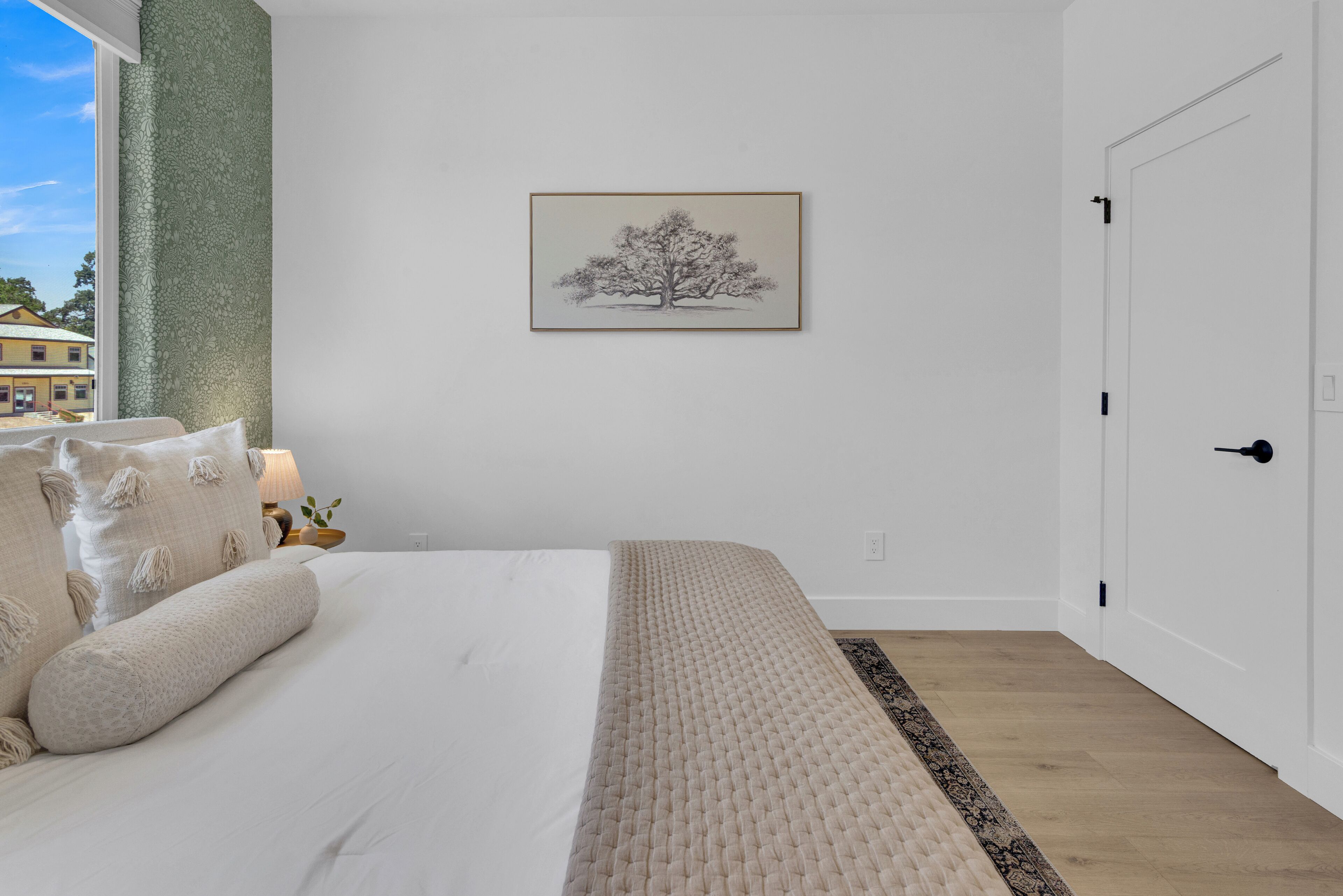 Un dormitorio con una cama grande, una mesita de noche con lámpara, un cuadro en la pared y una puerta.
