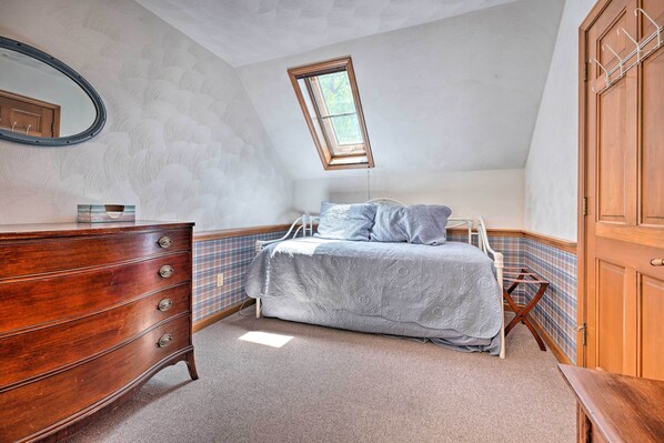 Ein Schlafzimmer mit einem Holzkapuzenpaneel, einem Bett mit grauer Bettdecke, einem Oberlicht und einem Holzschrank.