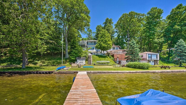 A wooden dock leading to a clear water body, surrounded by lush greenery and residential buildings. - Private Dock & Stunning Views: Corey Lake Getaway! (Three Rivers)