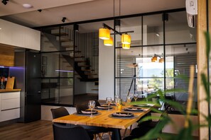 Un espace de salle à manger moderne avec une table en bois dressée pour six personnes, des chaises noires et des suspensions jaunes.