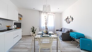A modern kitchen with white cabinets, a dining table with chairs, a chandelier, and a sofa in the living area. - Sunset Terrace Mazara - One bedroom flat with stunning  sea view rooftop (Mazara del Vallo)