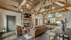 A spacious living area with a stone fireplace, wooden beams, and a large leather sofa. - Cozy lux retreat with VIEWS and hot tub (Ellijay)