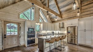 A spacious kitchen with wooden beams, a large island with bar stools, stainless steel appliances, and a view through the windows. - Cozy lux retreat with VIEWS and hot tub (Ellijay)
