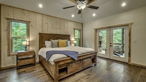 A bedroom with a wooden bed, nightstands, a ceiling fan, and large windows. - Cozy lux retreat with VIEWS and hot tub (Ellijay)