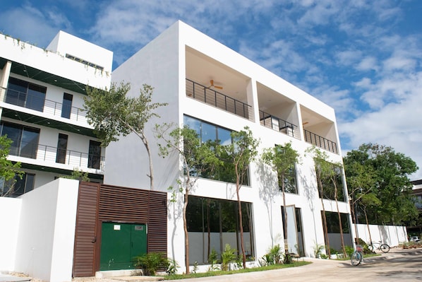 A modern multi-story building with balconies, large windows, and a green gate.