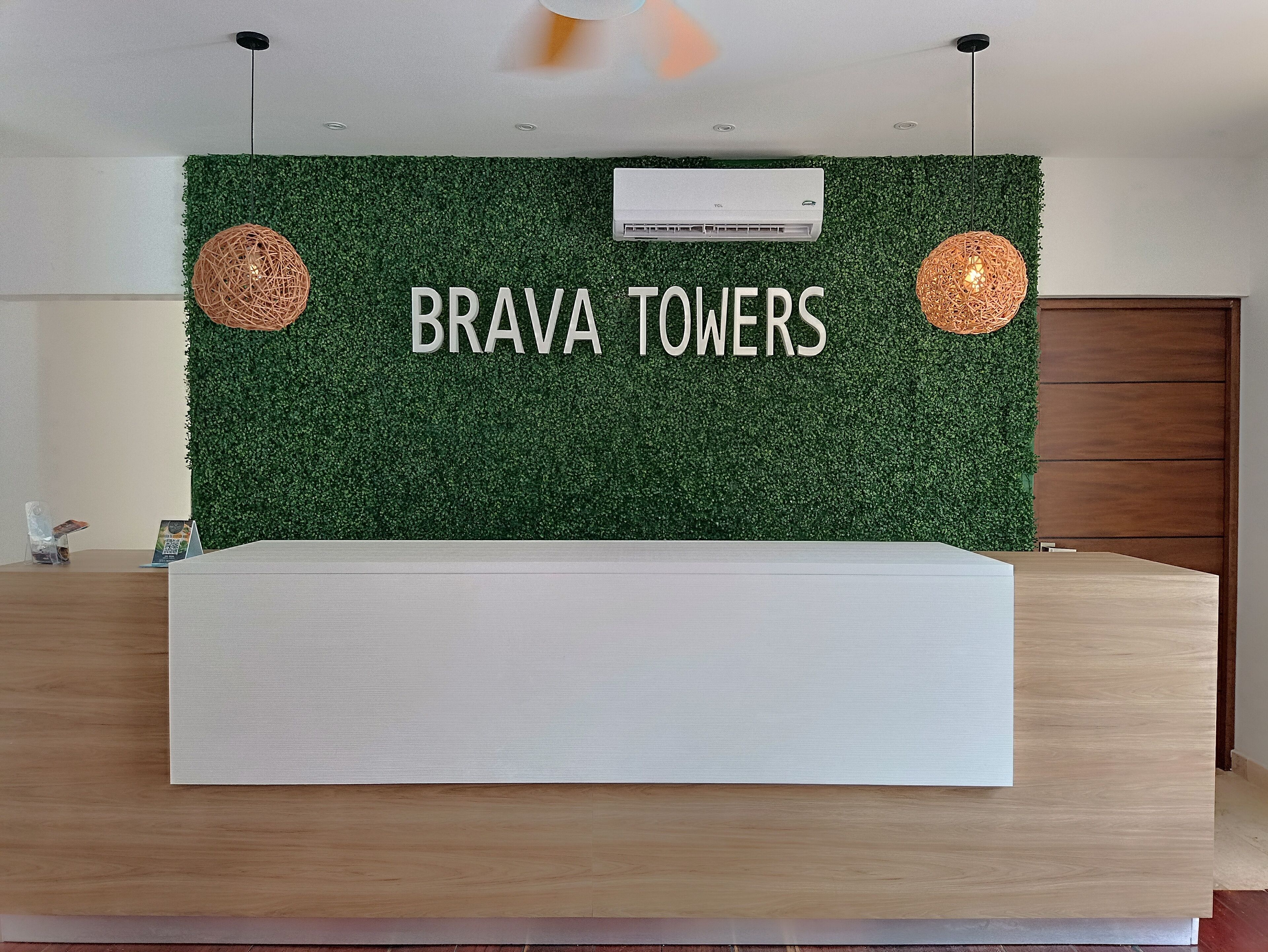 A reception desk with a green wall and the text "BRAVA TOWERS" in the background.