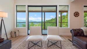 A modern living room with two white chairs, a dark leather sofa, and large windows offering a view of mountains and greenery. - Indoor Pool | Hot Tub | Game Room (Sevierville)