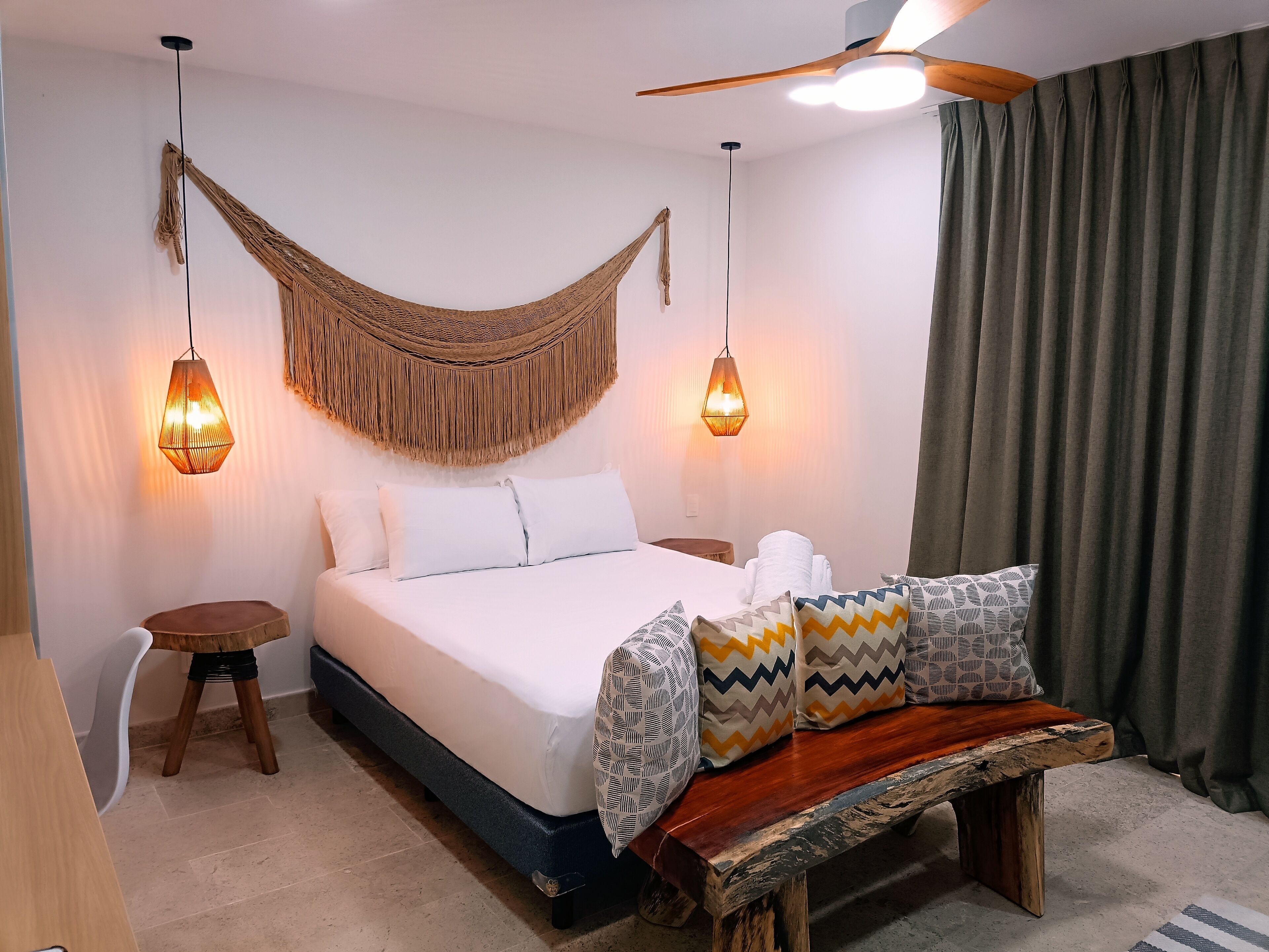 A bedroom with a bed, a wooden bench, a hanging hammock, and two pendant lights.