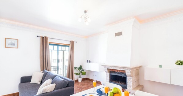 Una sala de estar moderna con un sofá gris, una mesa de comedor con alimentos para el desayuno y una chimenea.