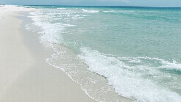 Ein Strand mit klarem türkisblauem Wasser und sandigem Ufer unter einem bewölkten Himmel.