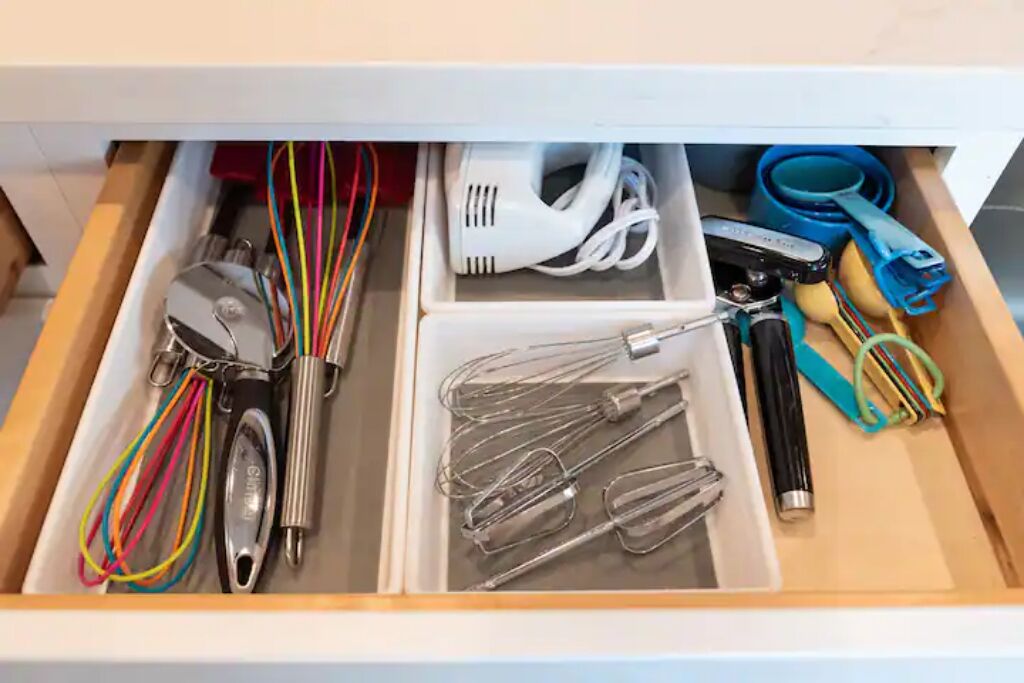 Uma gaveta com utensílios de cozinha, incluindo batedores, batedeira e processador de alimentos.