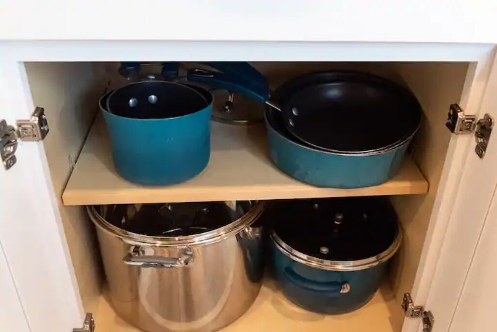 Ein Küchenschrank mit zwei Regalen, auf denen Töpfe und Pfannen stehen.