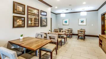 A dining area with multiple tables and chairs, framed artwork on the walls, and a herringbone floor pattern.