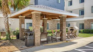 An outdoor patio area with stone pillars, a grill, and seating.