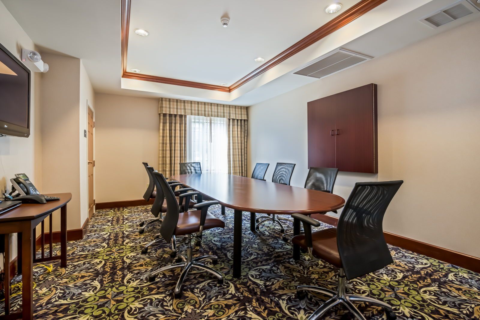 A conference room with a long table, six chairs, a flat-screen TV, and a telephone on a desk.