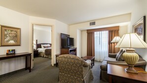 Habitación de hotel con sofá, sillón, televisor, lámpara y un cuadro en la pared.