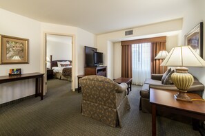 Habitación de hotel con sofá, sillón, televisor, lámpara y un cuadro en la pared.