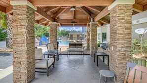 Un patio exterior con pilares de piedra, piscina y zona de barbacoa.
