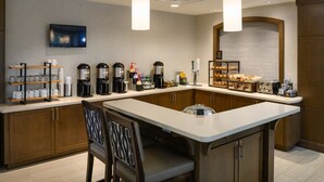 Una cucina moderna con isola centrale, macchine da caffè, televisore e bancone colazione.