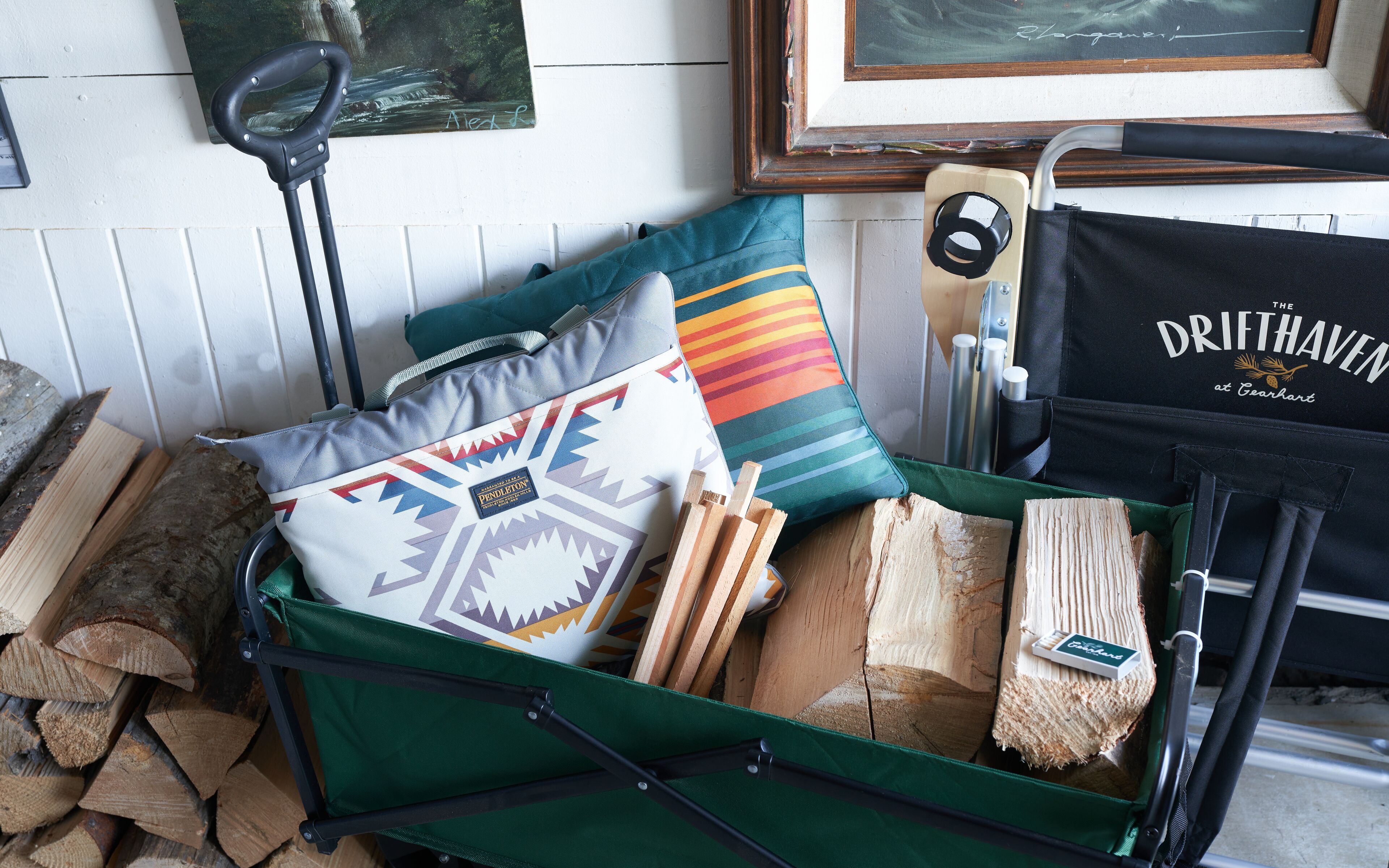 Une valise verte remplie de bois, un coussin aux couleurs vives et un sac noir sur lequel on peut lire : « The Drifthaven at Gearhart ».