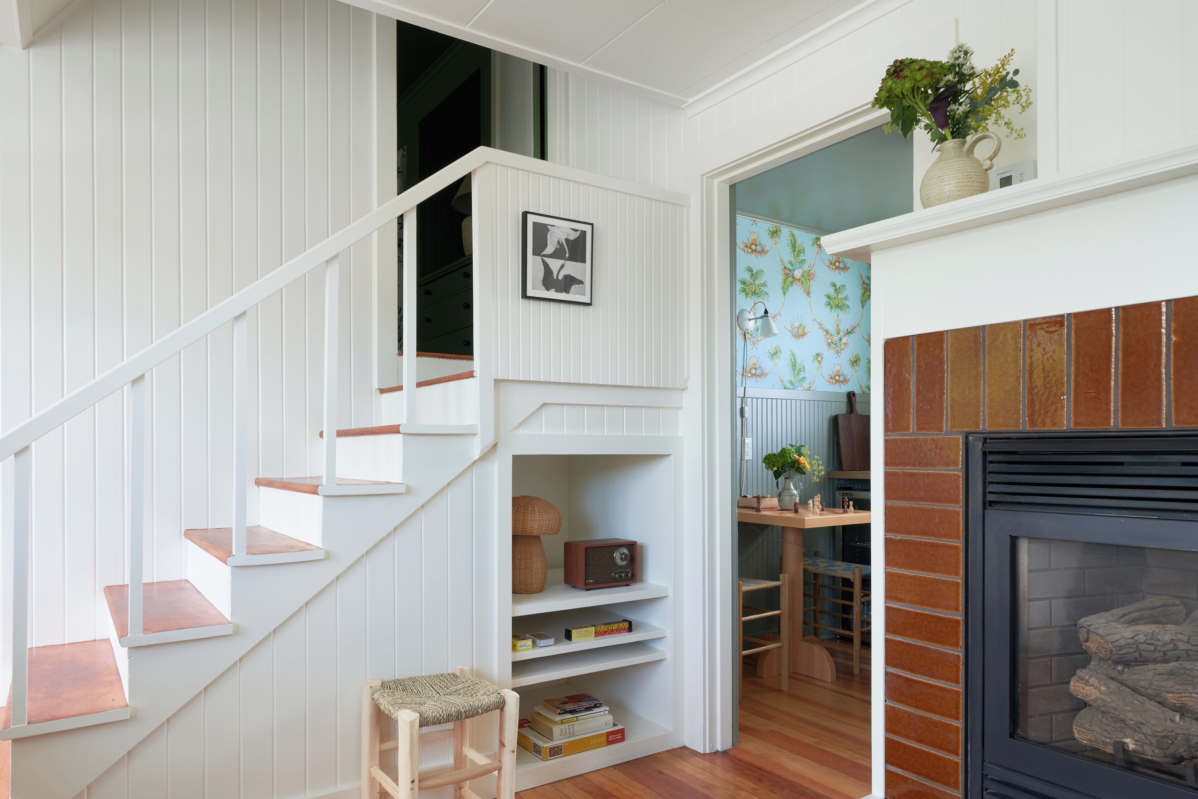Una escalera con barandillas blancas y escalones de madera que conduce a un rellano con una estantería y un sillón pequeño.