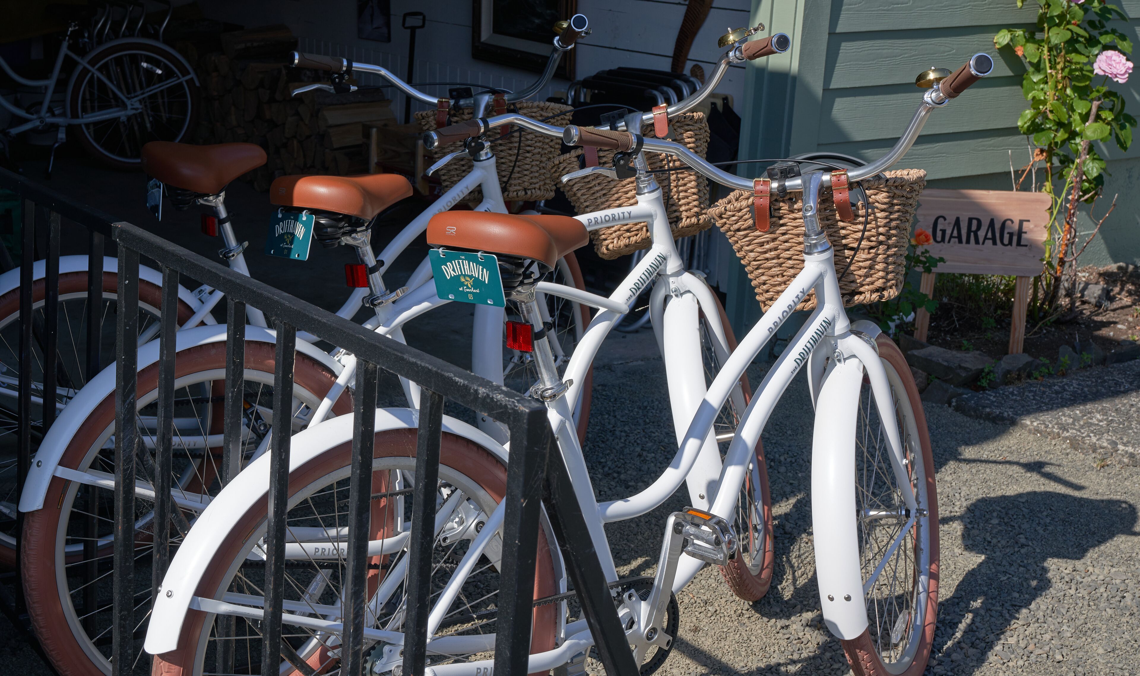 Una bicicleta blanca con asientos de cuero marrón y una canasta, estacionada frente a un letrero de madera que dice "GARAGE".
