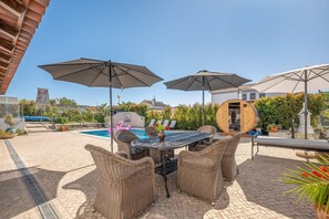 Un espace aménagé au bord de la piscine, avec des meubles en osier, des parasols et un tonneau en bois.