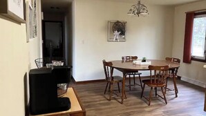 Un coin repas avec une table ronde et des chaises en bois, un lustre et une petite plante posée sur la table.