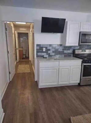 Compact kitchen area with a flat-screen TV, stainless steel oven, and tiled backsplash.