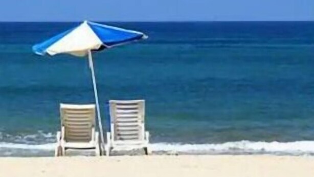 En strandscen med två vita solstolar och ett blått och vitt strandparasoll.