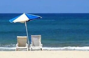 A beach scene with two white lounge chairs and a blue and white beach umbrella. - Beach and downtown Hollywood (Hollywood)
