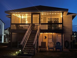 A two-story house with a balcony, a staircase, and string lights. - MoreBeachTime
Great Location 
Family's & pets
Open Mid-week 8/19-22
& 8/24 > 9/5 (Kill Devil Hills)