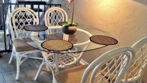 A round glass table with woven chairs, a potted plant, and a hanging ornament. - Labor Day Week (9/3-9/10) Ocean Resort Condo (Hilton Head Island)