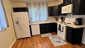 A compact kitchen with a refrigerator, microwave, stove, and black cabinets. - The Jacks Fork Town House in Eminence (Eminence)