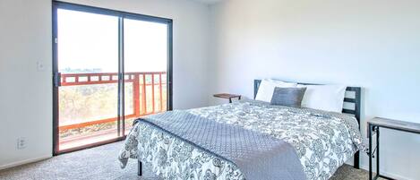 A bedroom with a large bed, a nightstand, a window with a view, and a sliding door to a balcony.